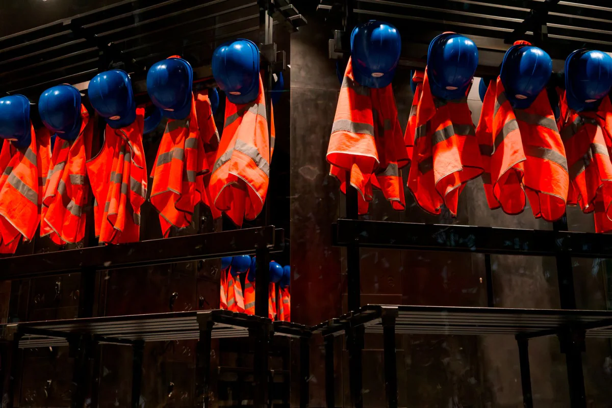 Orangefarbene Warnjacken und blaue Helme hängen in einer Reihe