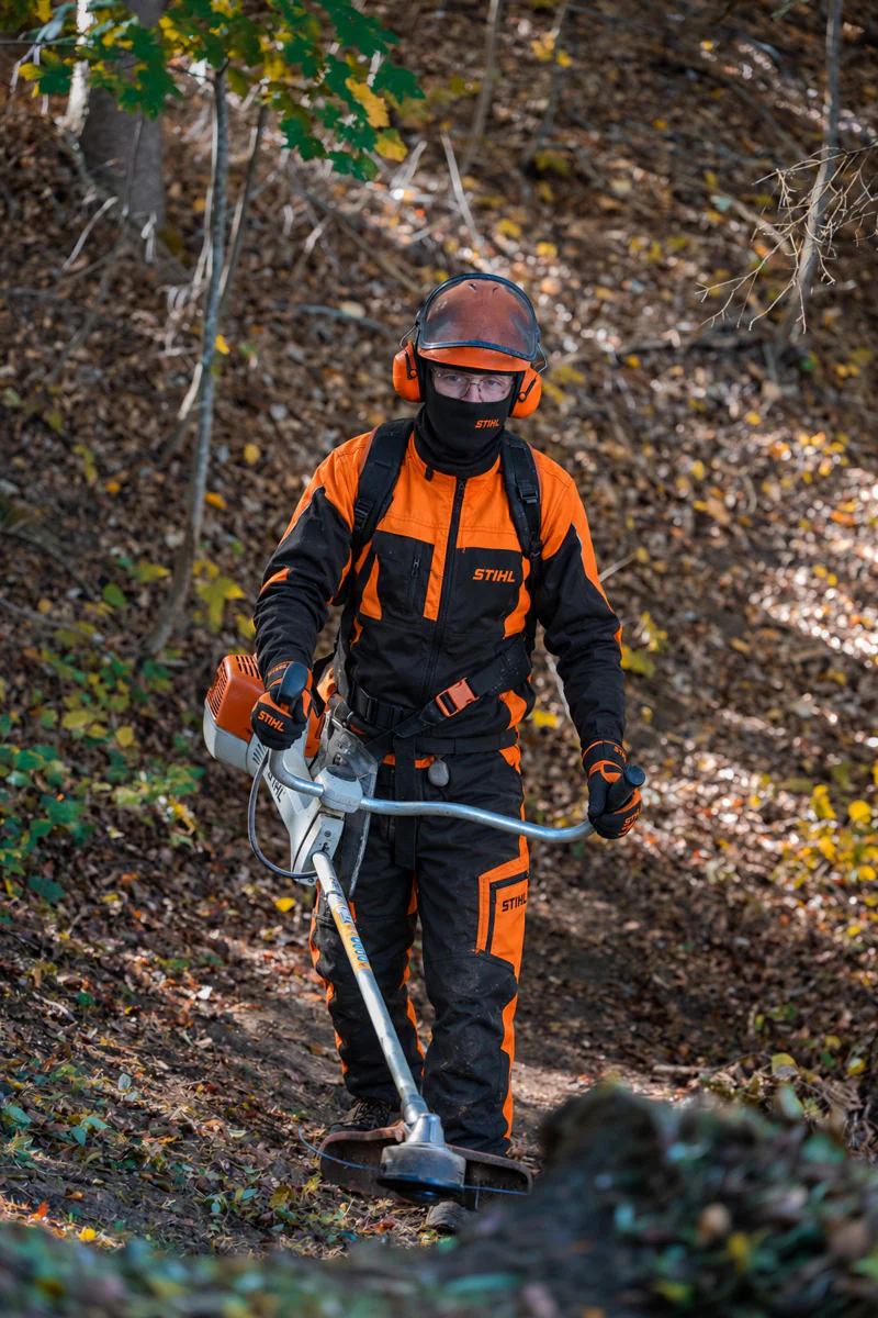 Arbeiter in oranger Schutzkleidung mit Freischneider im Wald