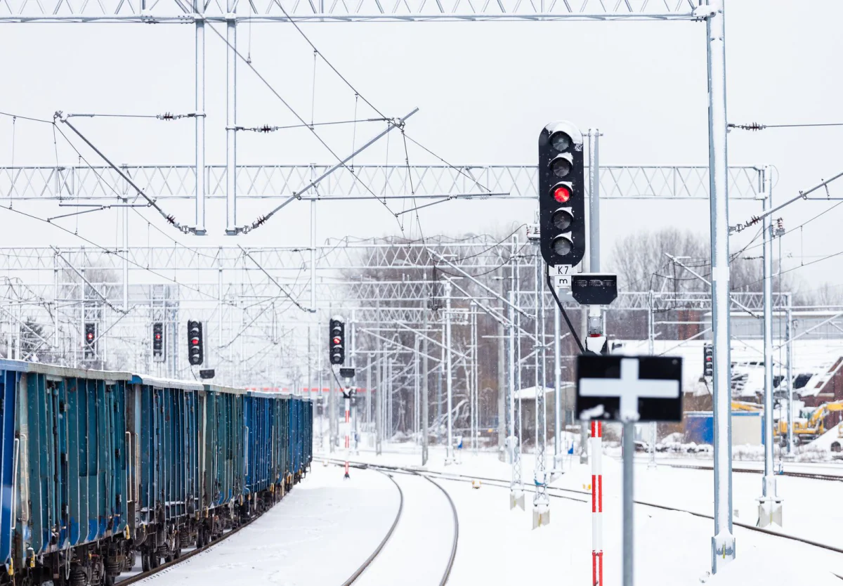 Verschneites Gleisfeld mit Oberleitung, Lichtsignal und abgestellten Güterwagen