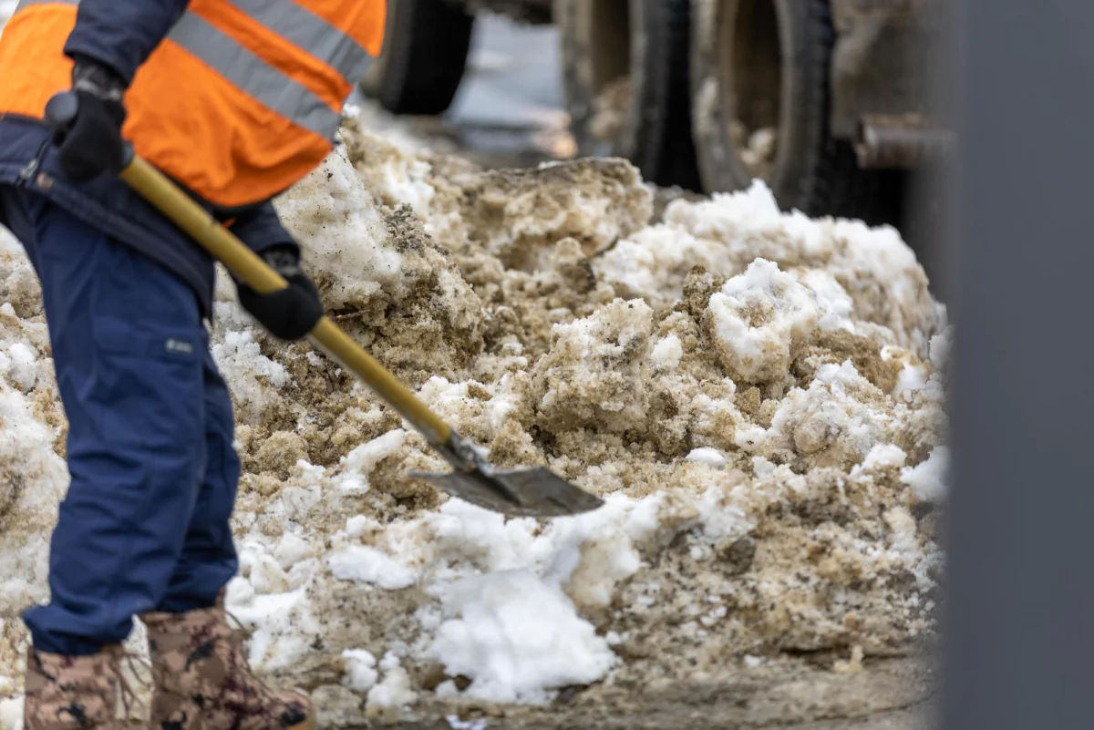 Arbeiter in Warnkleidung schaufelt Schnee von einer Fläche